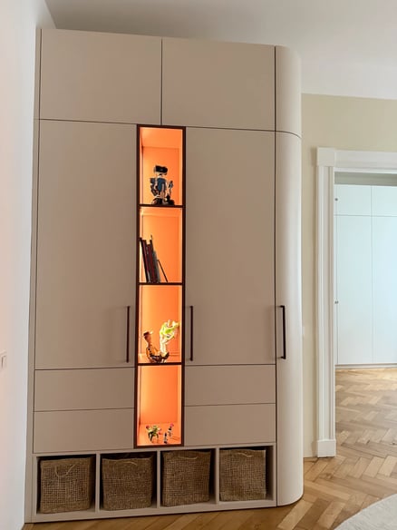 Béžová skříň s osvětlenými nikami a proutěnými košíky.